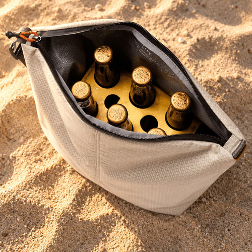 A cooler bag in light grey containing six dark bottles, set against a sandy background.