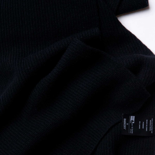 A textured black Merino wool scarf, featuring a label, displayed on a white background. A textured black Merino wool scarf, featuring a label, displayed on a white background.