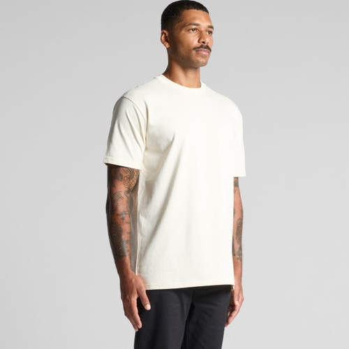 A light cream classic tee shirt displayed on a model with tattoos, featuring a simple design and a logo.