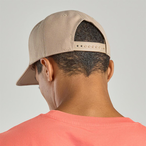 A beige cap is worn backwards by a person, showcasing its adjustable strap on the back. A beige cap is worn backwards by a person, showcasing its adjustable strap on the back.