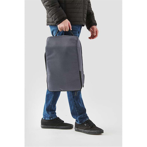 A person carrying a grey Toluca Backpack with a handle, wearing dark jeans and black shoes. The backpack has a logo.