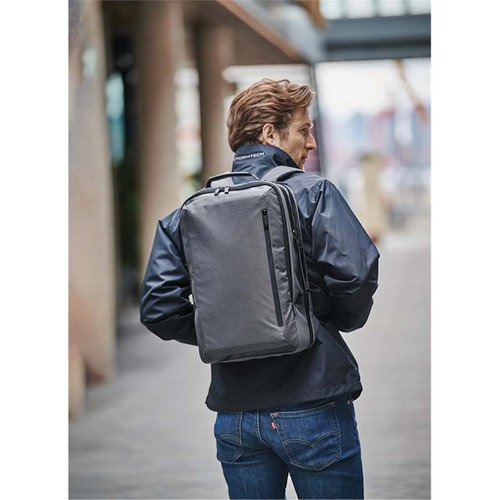 A person wearing a black jacket carries a grey Hedmark Commuter Backpack on their back in an outdoor setting.
