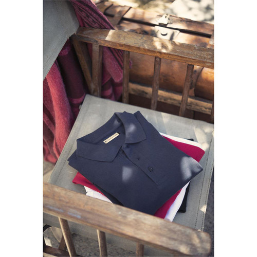 A navy men's cotton polo shirt rests neatly on a wooden chair, alongside a red and a white folded shirt. A navy men's cotton polo shirt rests neatly on a wooden chair, alongside a red and a white folded shirt.