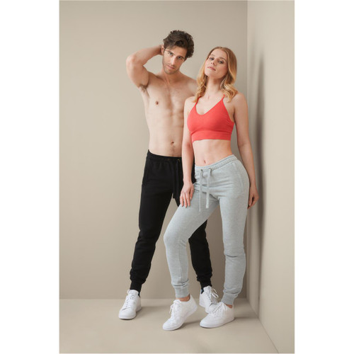 A pair of unisex sweatpants in black and grey, styled with a model wearing a red crop top. Both models are standing. A pair of unisex sweatpants in black and grey, styled with a model wearing a red crop top. Both models are standing.