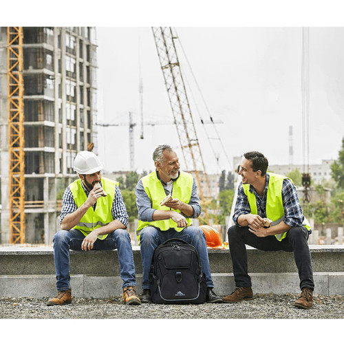 Three men in reflective vests sit together on a construction site, discussing beside a black High Sierra Access 4.0 Backpack.