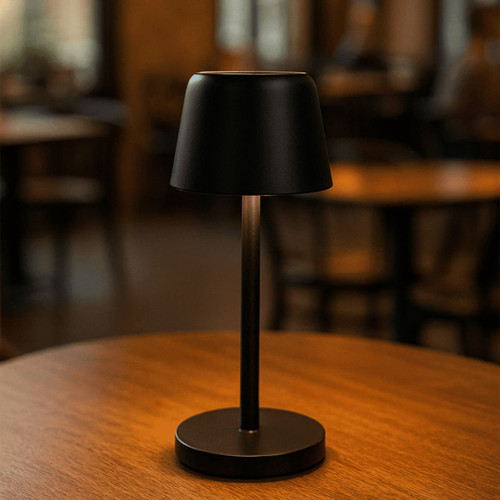 A black mini rechargeable lamp with a tapered shade, standing on a circular base, placed on a wooden table.