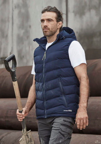Unisex hooded puffer vest in navy, featuring a zipper and a logo, modelled by a man holding a shovel outdoors. Unisex hooded puffer vest in navy, featuring a zipper and a logo, modelled by a man holding a shovel outdoors.