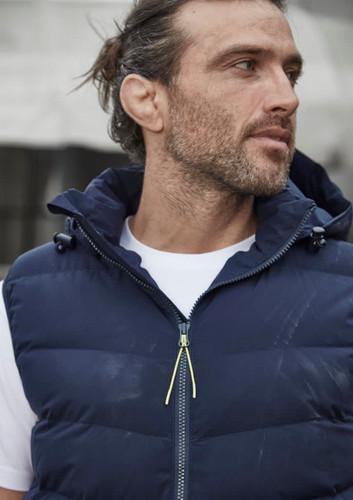 A unisex hooded puffer vest in navy blue, featuring a zip front and a hood, displayed on a model. A unisex hooded puffer vest in navy blue, featuring a zip front and a hood, displayed on a model.