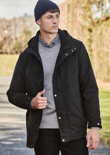 A model wearing a black jacket and a navy beanie, standing outdoors with greenery in the background.