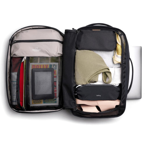 A black backpack with various items packed inside, including clothing, a laptop, and storage pouches in neutral tones. A black backpack with various items packed inside, including clothing, a laptop, and storage pouches in neutral tones.