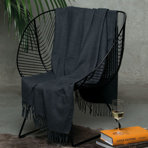 A dark grey merino blanket draped over a modern black chair, with a glass of wine and books nearby. A dark grey merino blanket draped over a modern black chair, with a glass of wine and books nearby.