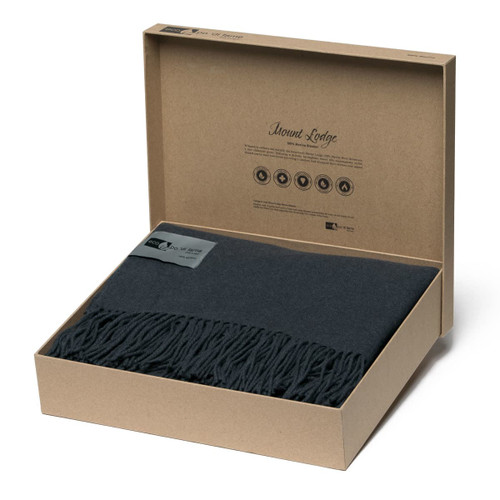A dark grey Merino blanket with a fringed edge, presented in a stylish brown box with branding. A dark grey Merino blanket with a fringed edge, presented in a stylish brown box with branding.