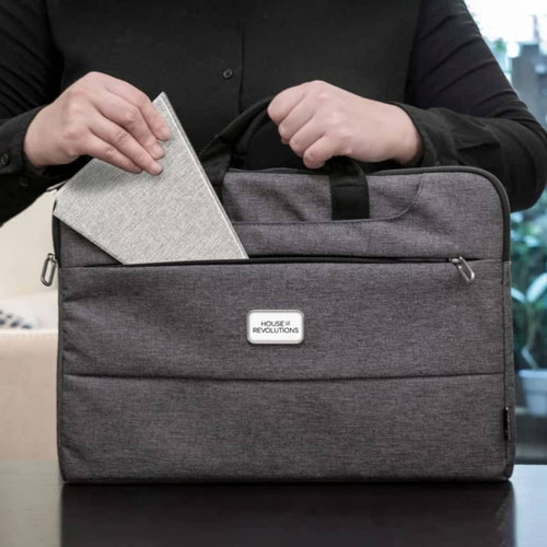 A grey laptop bag with a front pocket, being opened to reveal a notebook inside. The bag features a logo. A grey laptop bag with a front pocket, being opened to reveal a notebook inside. The bag features a logo.