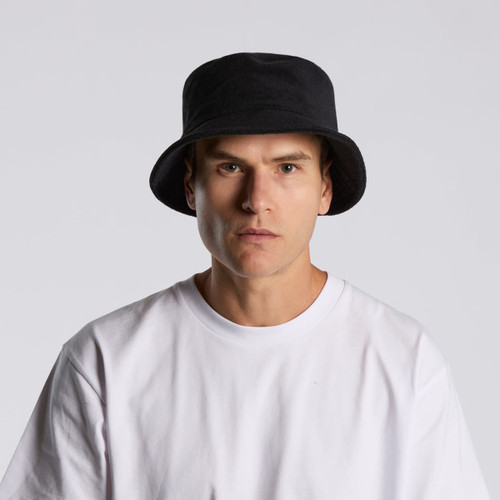 A black Terry Bucket Hat displayed on a model wearing a white t-shirt. The hat features a logo. A black Terry Bucket Hat displayed on a model wearing a white t-shirt. The hat features a logo.