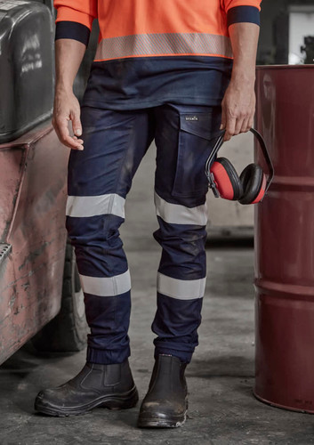 A pair of navy women's cargo pants with reflective stripes, cuffed at the ankles, held by a person wearing work boots. A pair of navy women's cargo pants with reflective stripes, cuffed at the ankles, held by a person wearing work boots.
