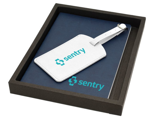 A navy notebook and white luggage tag with a branding logo, presented in a dark box. A navy notebook and white luggage tag with a branding logo, presented in a dark box.