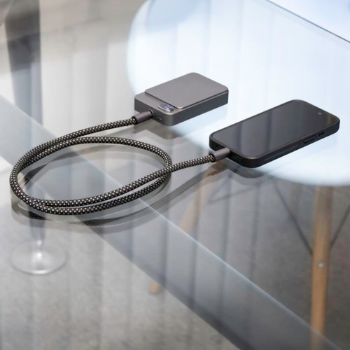 A fast charge cable in black with a textured design, connected to a phone and a charging device on a glass surface. A fast charge cable in black with a textured design, connected to a phone and a charging device on a glass surface.