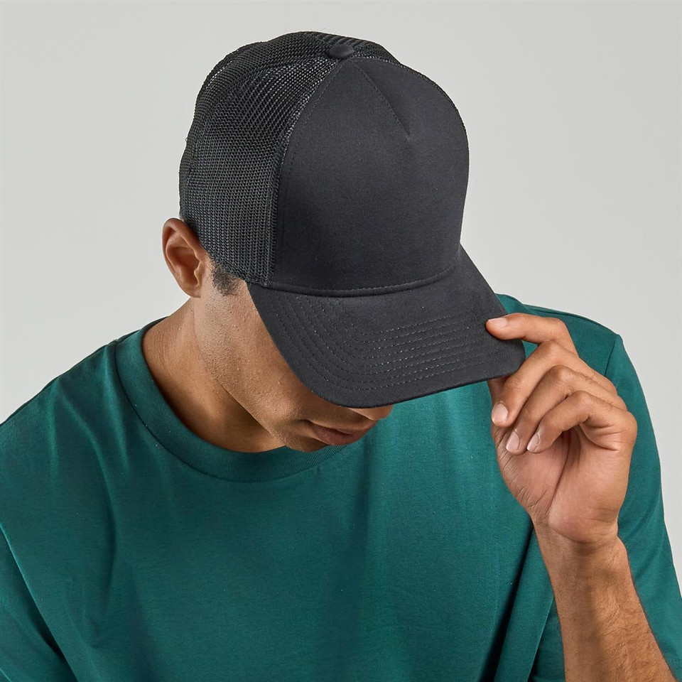 A black trucker cap with a mesh back, worn by a person in a teal shirt. The cap features a logo on the front.