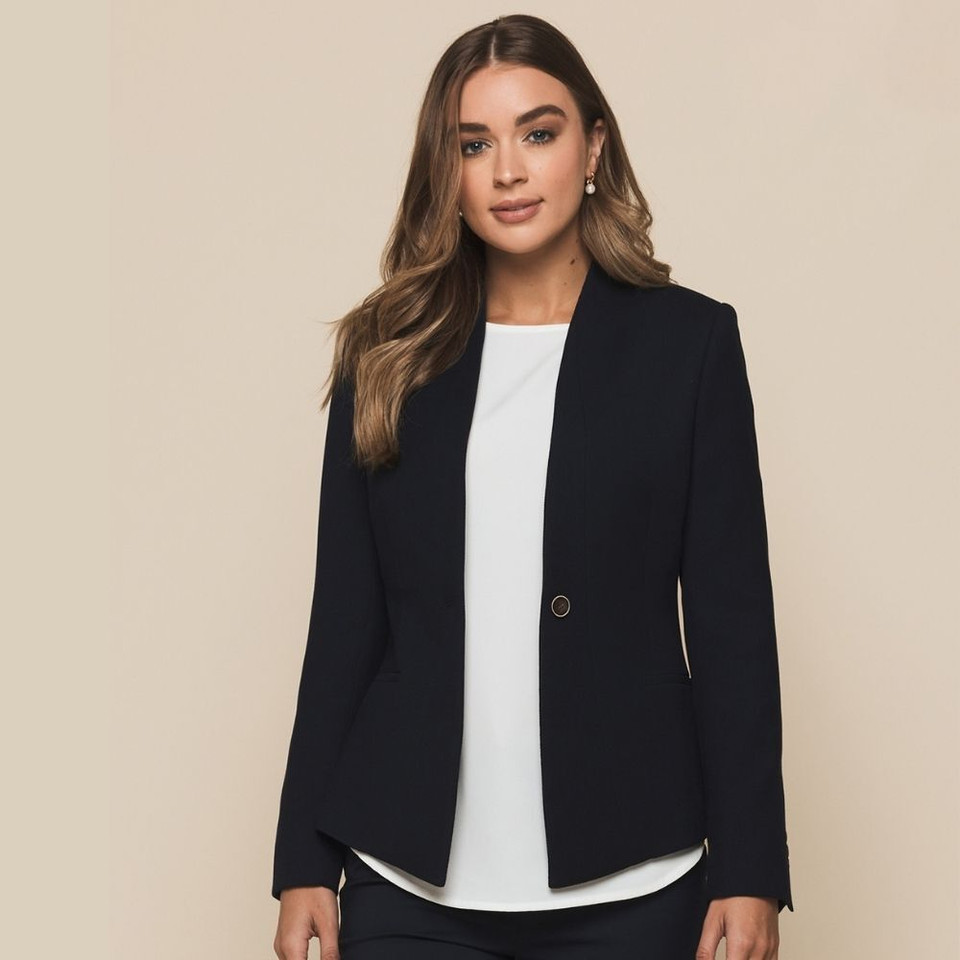 A woman wearing a white top and a navy crop suit jacket featuring a single button closure and long sleeves, with a branded label inside.