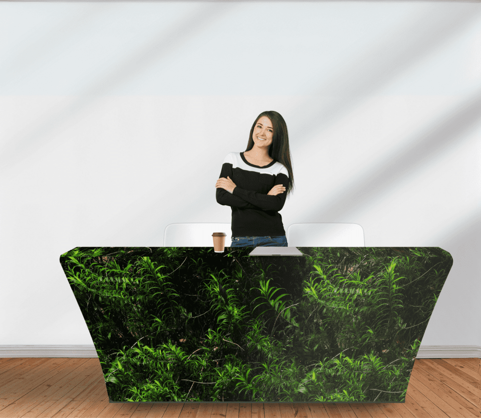 A woman stands behind a green rPET stretched table cover, featuring a leafy design, on a wooden floor.
