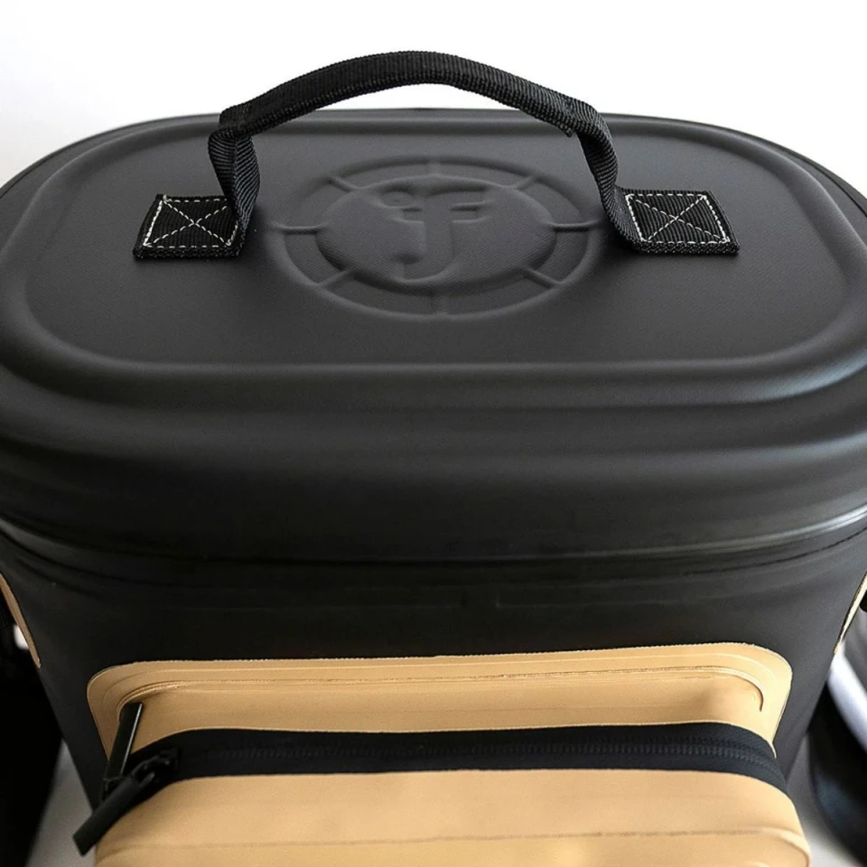 Close-up view of the Fridgy cooler bag featuring a reinforced top carry handle, waterproof lid, and front zippered accessory pocket in a black and tan colorway.