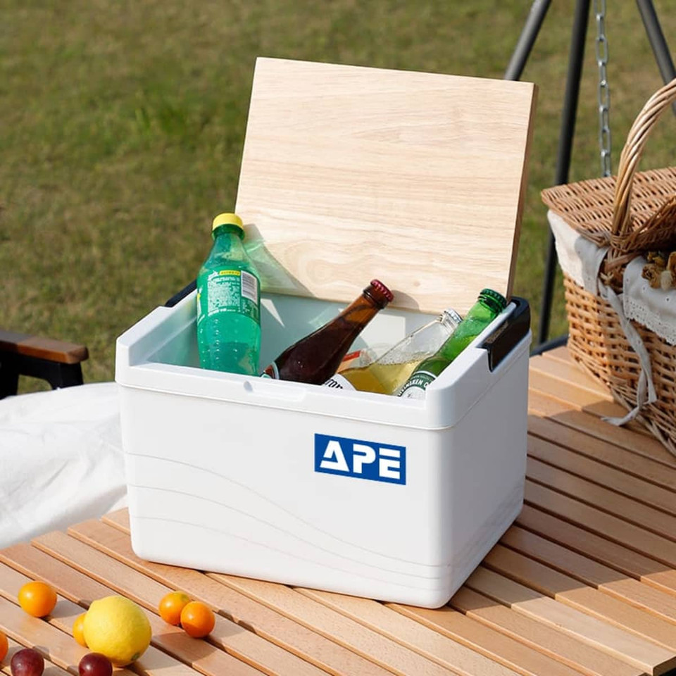 A white cooler box with a wooden lid, filled with various beverage bottles, sits on a table outdoors.