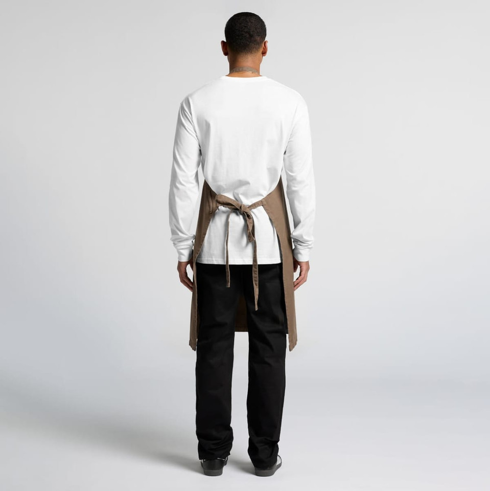 A person wearing a beige canvas apron over a white long-sleeve shirt and black pants, viewed from the back.