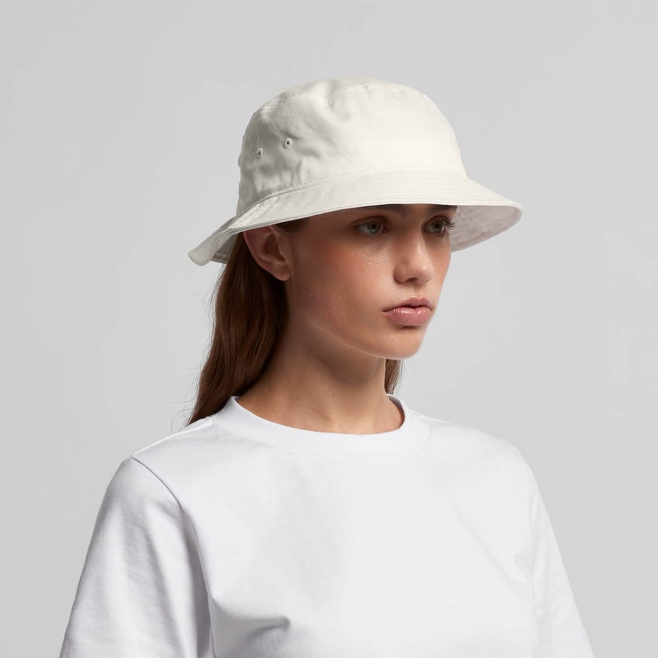 A white bucket hat with a wide brim, featuring ventilation holes and a logo. Worn by a model in a plain white t-shirt.