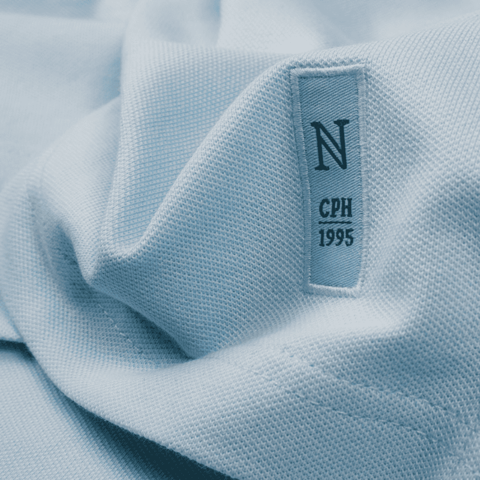 A detailled photograph of the seam of a light blue polo shirt with a logo embroidered on it.