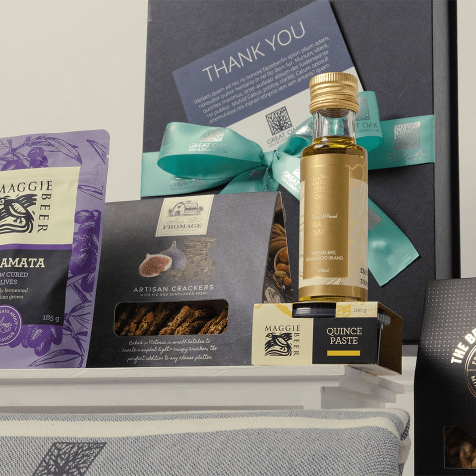 A gourmet gift pack featuring a bottle of quince paste, artisan crackers, and assorted treats in purple and black packaging.