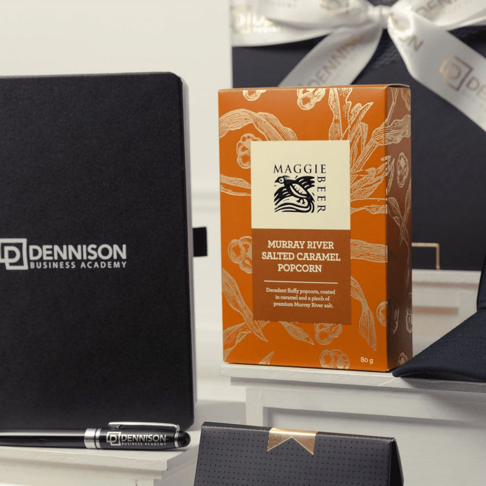 A gift pack featuring a black notebook, a silver pen, a black cap, and orange popcorn packaging.