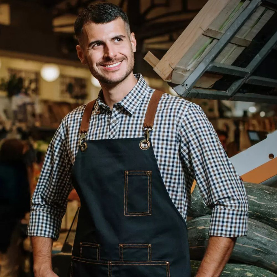 A man with short dark hair smiling, wearing a black apron, his hands on his hips