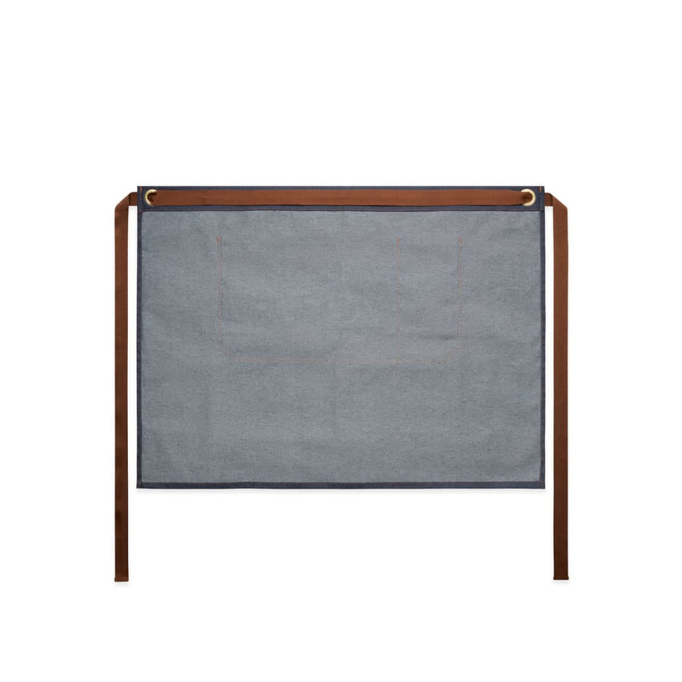 A denim half apron in blue with brown ties, featuring two pockets and a branded logo.