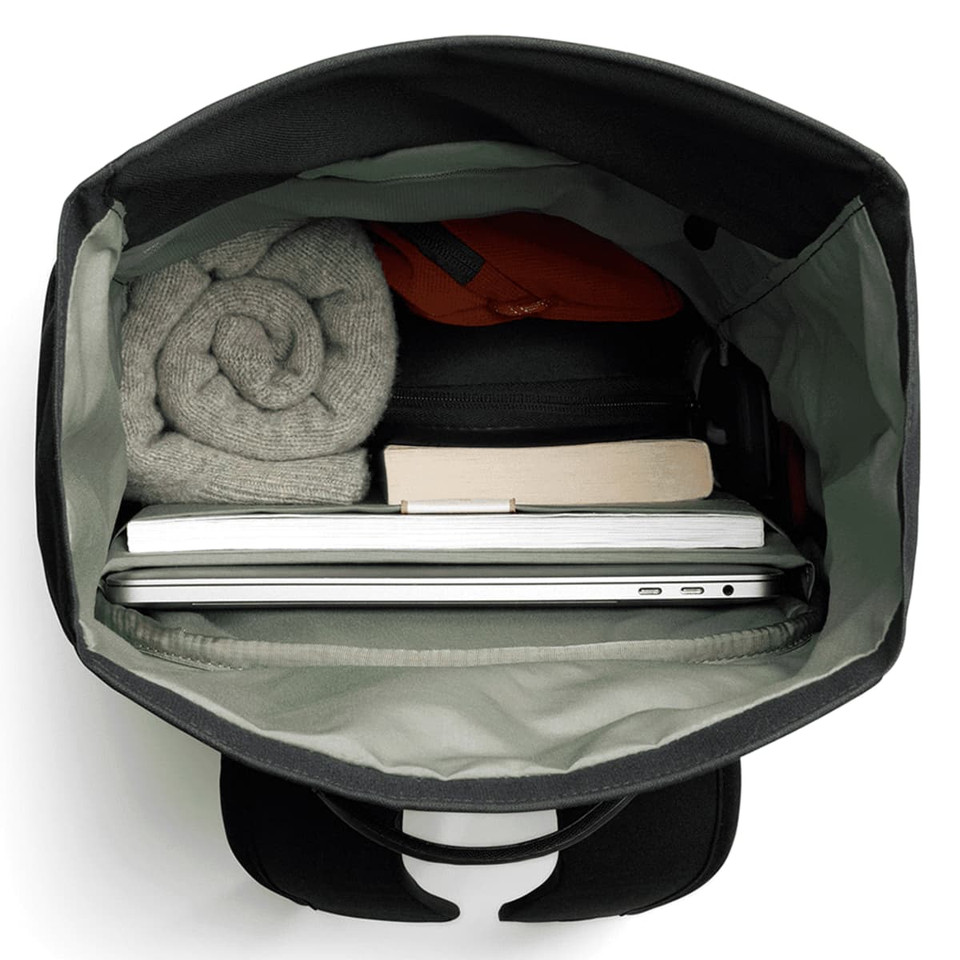 A black rolltop bag with a grey interior, containing a laptop, a book, and rolled clothing.