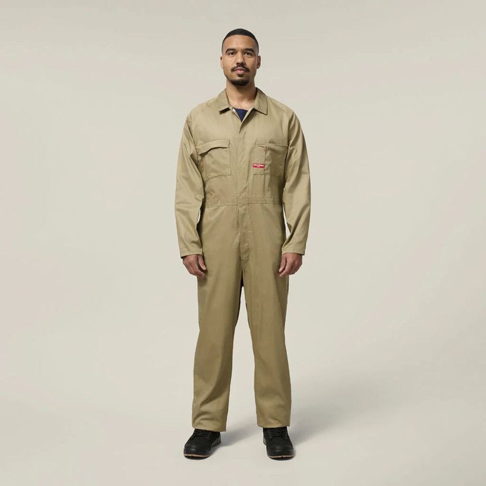 Male model wearing a khaki work jumpsuit and black work boots against a neutral background.