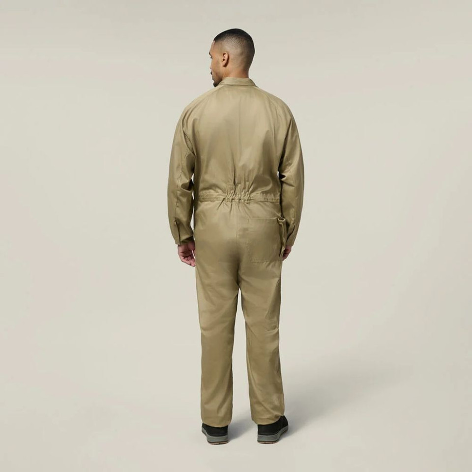 Back view of male model wearing a khaki work jumpsuit and black work boots against a neutral background.