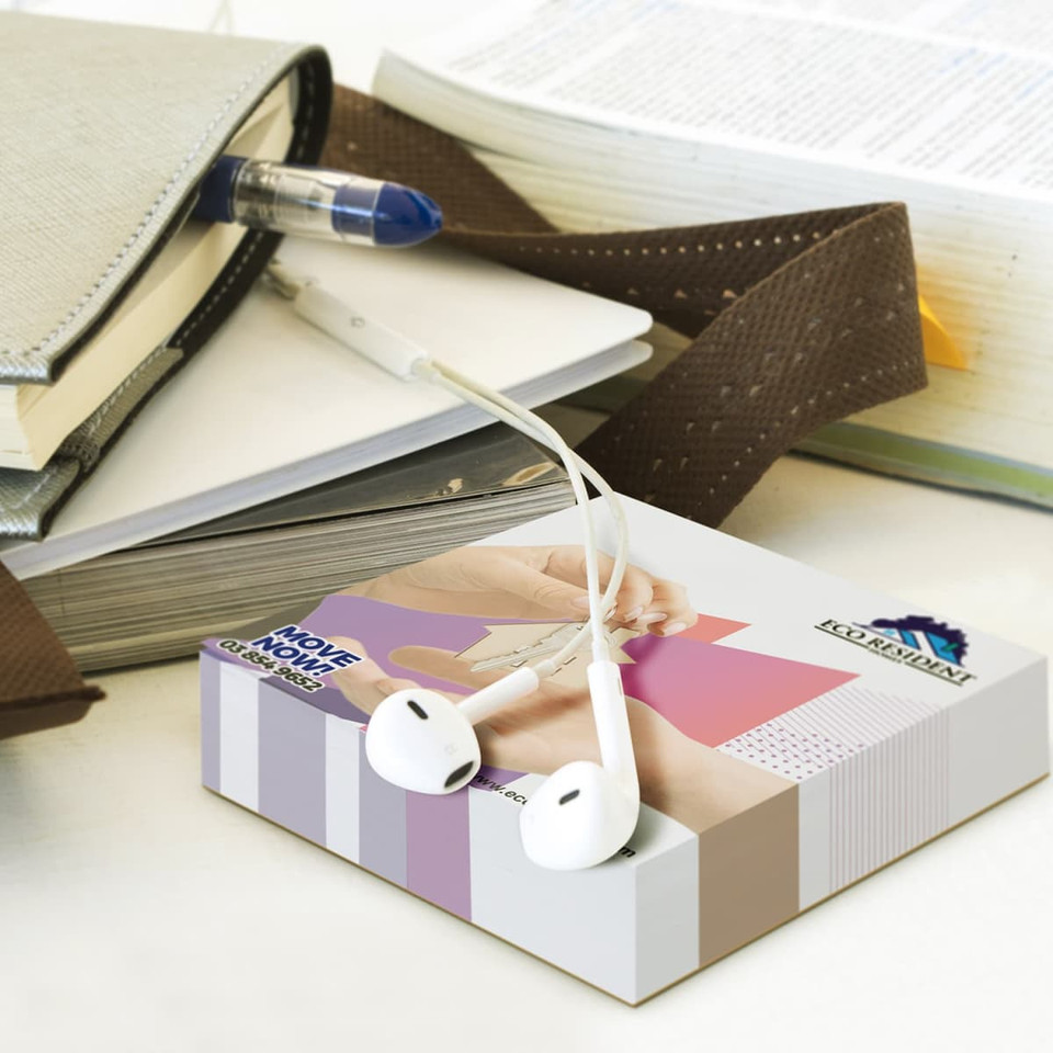 A memo cube notepad in white with earphones resting on top, surrounded by stationery and a book.
