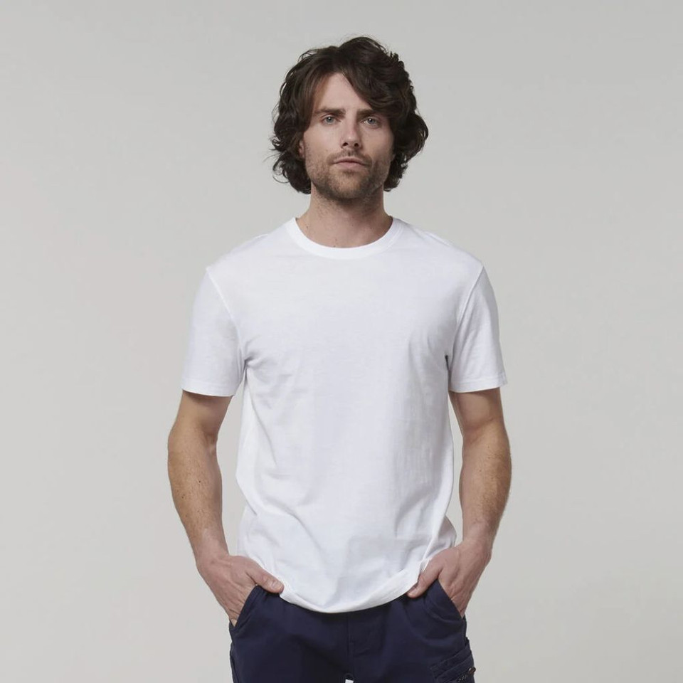 Man wearing a plain white t-shirt with hands in pockets against a neutral background