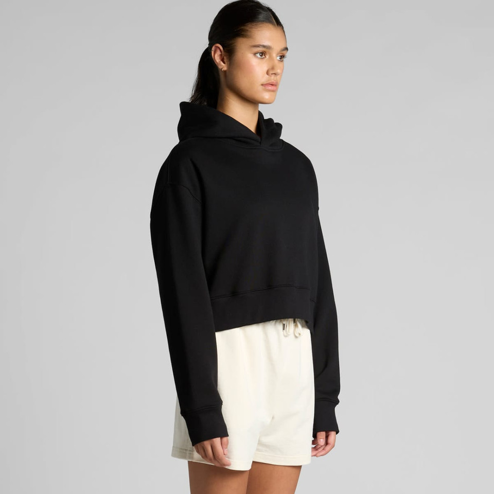 A black cropped hoodie with a relaxed fit, featuring a hood and long sleeves, paired with light-coloured shorts.