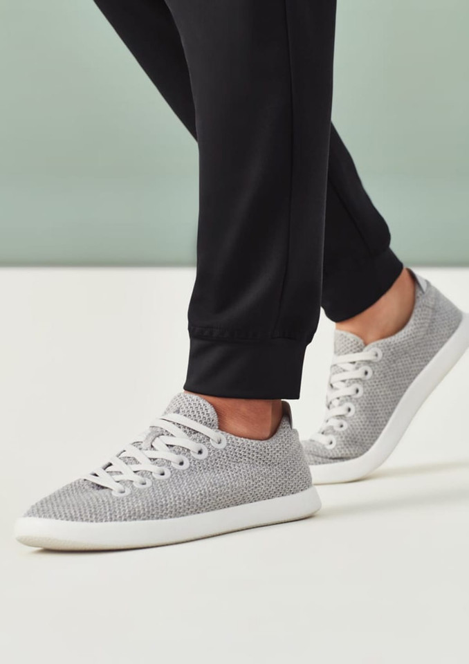 A pair of grey sneakers worn with black jogger scrub pants, featuring a smooth finish and elastic cuffs.