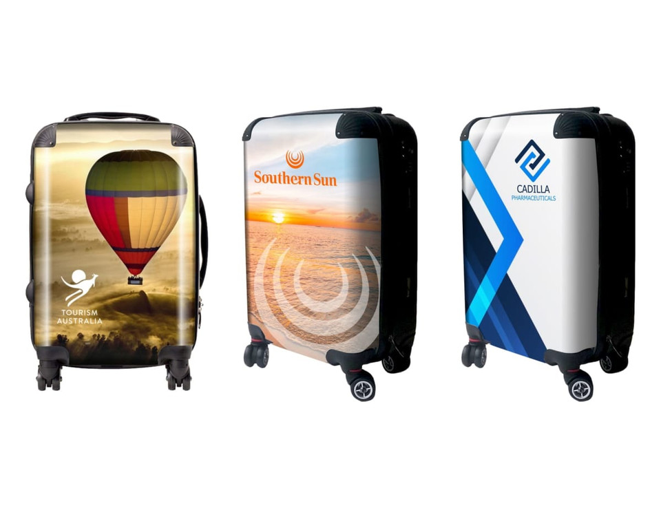 Three wheeled carry-on suitcases featuring colourful designs, including a hot air balloon, sunset, and abstract patterns.