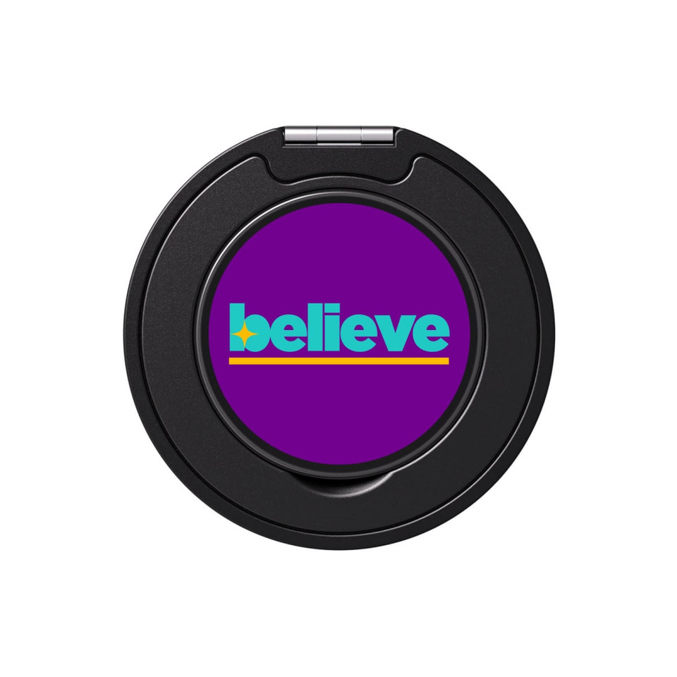 A round phone grip and stand in black with a vibrant purple centre featuring the word "believe" in green and yellow.