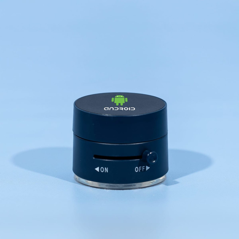 A black and silver device with a logo on top and a dial on the side, resting on a blue background.