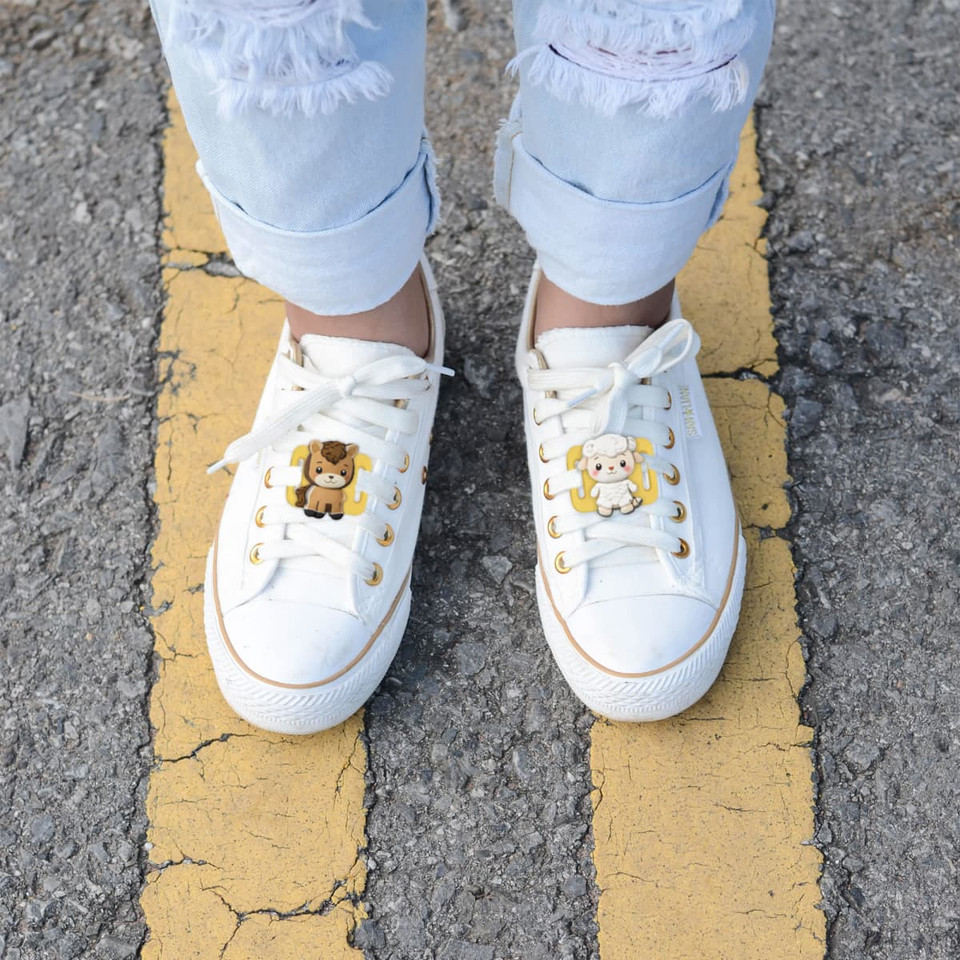 White sneakers adorned with novelty glowing clog shoe charms featuring a bear and a cow, set on a paved surface.