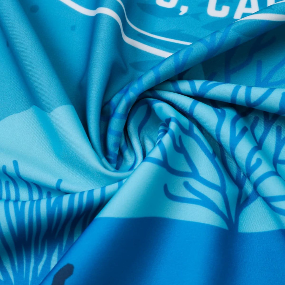 A blue sublimation fabric featuring intricate patterns resembling coral and sea life, with a logo in the design.