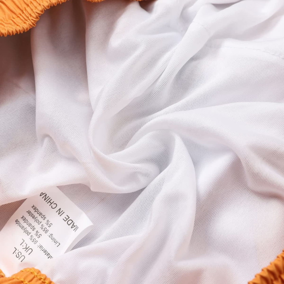 Close-up of the inner lining of orange board shorts, featuring a white, smooth fabric and a label.