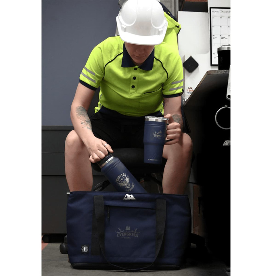 A blue drink bottle and mug sit next to a dark blue duffel bag, with a person in a high-visibility shirt and helmet.