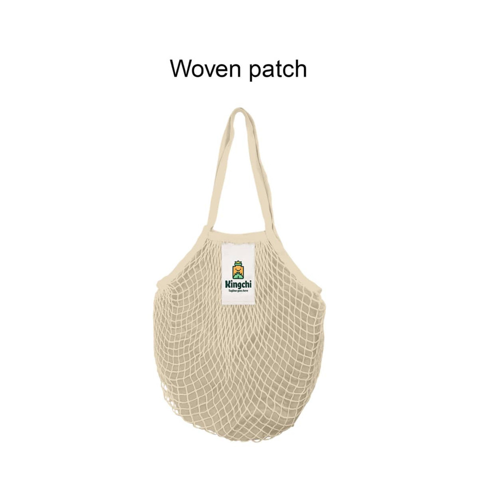 A beige mesh grocery bag with a woven patch and logo, featuring two handles for easy carrying.