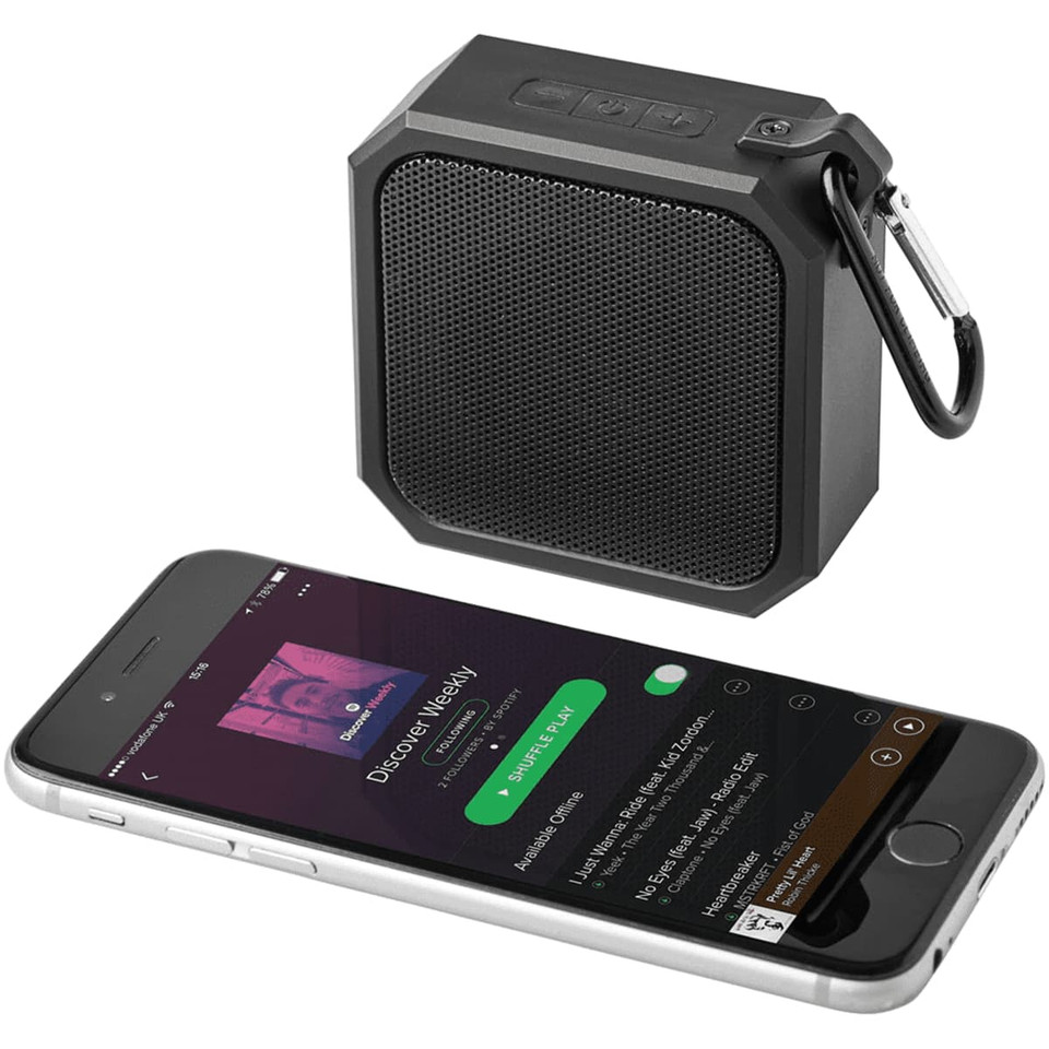 A black waterproof Bluetooth speaker with a textured mesh front and a carabiner, next to a smartphone displaying music.