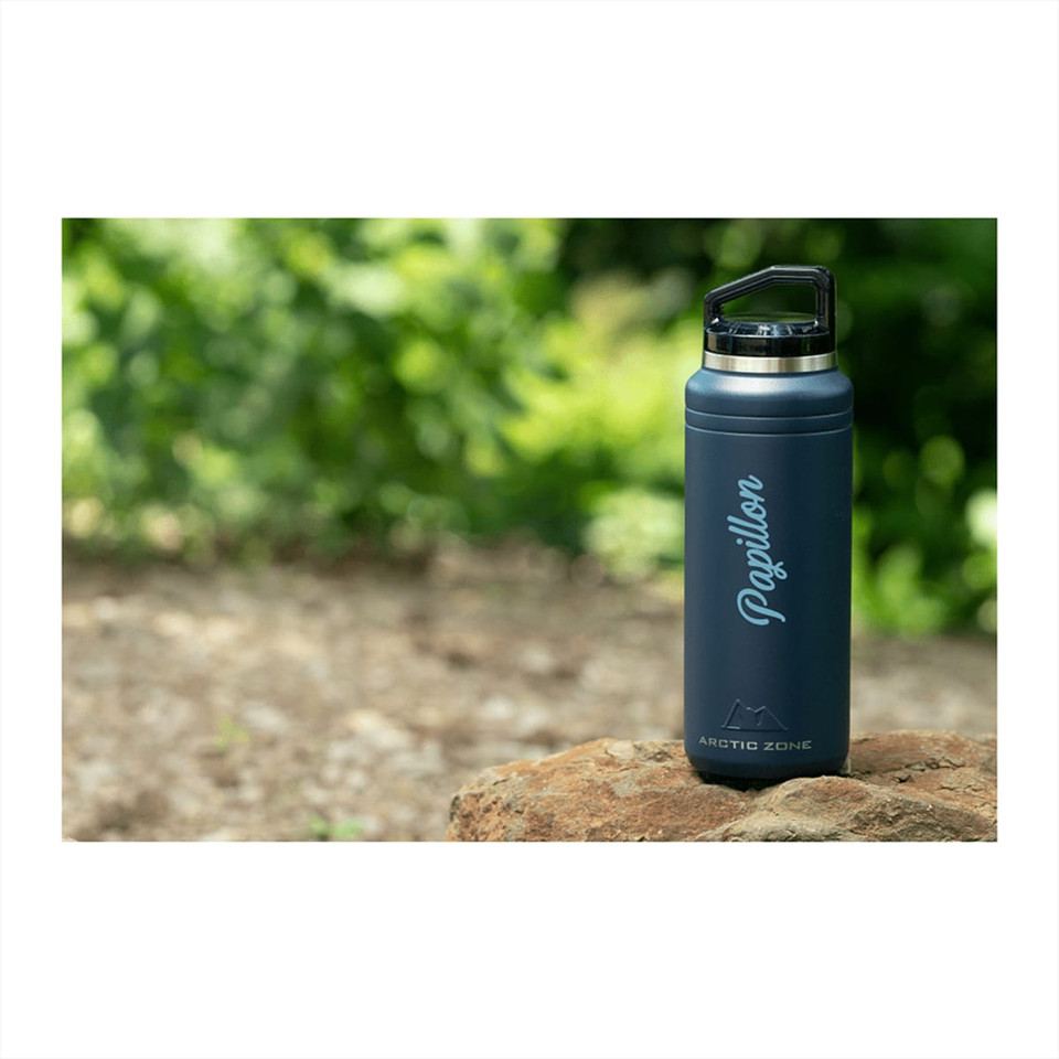 A drink bottle in dark grey, featuring a screw-on lid and a logo, set against a natural outdoor background.